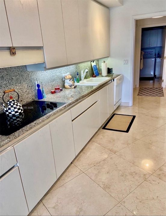Kitchen featuring flat-panel cabinetry, stone-finish countertops, integrated cooktop, undermount sink, and large-format tile flooring