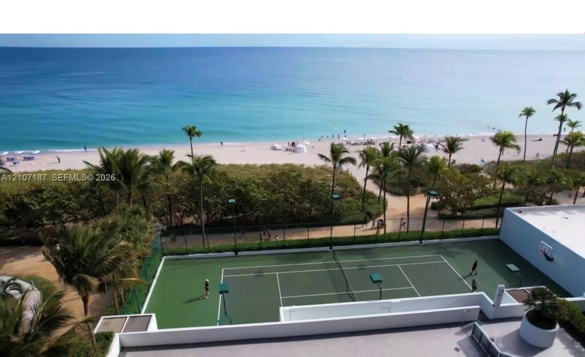 Tennis court featuring a hard surface, perimeter fencing, and integrated lighting fixtures, situated on the oceanfront