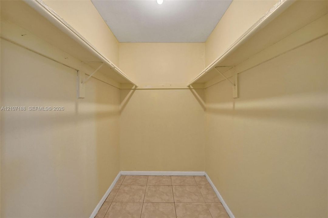Walk-in storage space featuring built-in shelving, hanging rods, and tile flooring