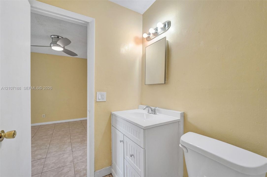 Bathroom featuring a white vanity cabinet with beadboard paneling, an integrated white sink, a chrome faucet, a wall-mounted medicine cabinet, and a multi-bulb vanity light fixture