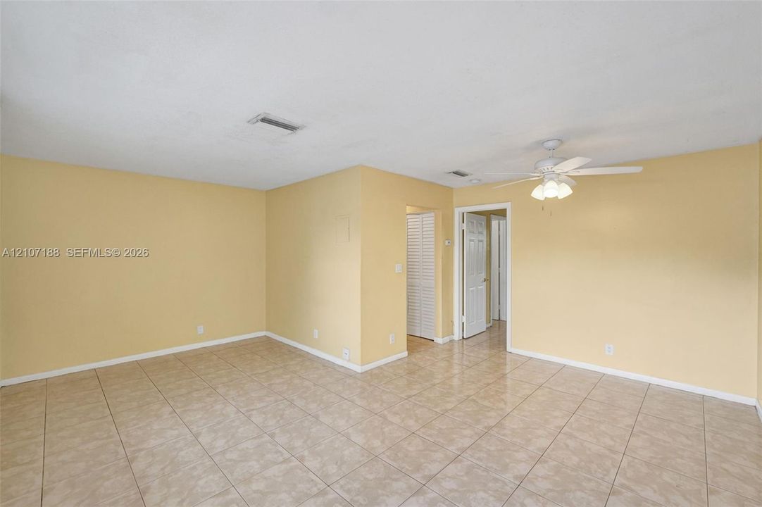 Interior room featuring neutral-toned tile flooring, light-colored walls, a ceiling fan with integrated lighting, and louvered bifold closet doors