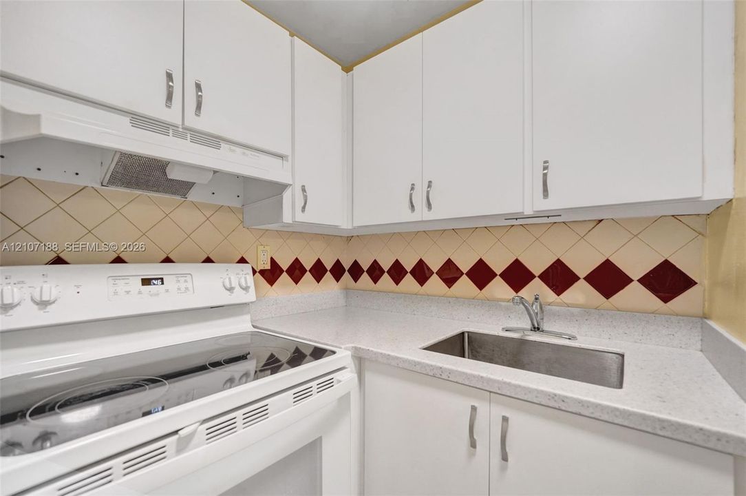Kitchen featuring white cabinetry, solid-surface countertops, a stainless steel undermount sink, and a range with a built-in ventilation hood