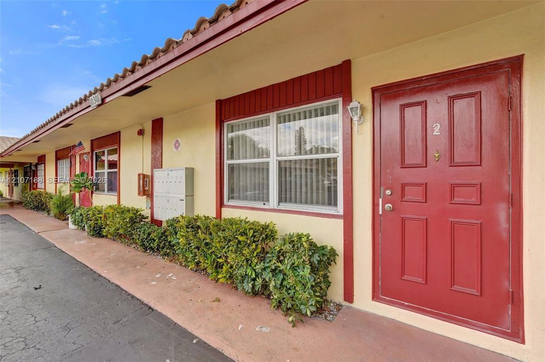 Stucco exterior featuring clay tile roof accents, red-toned paneled entry doors, and wall-mounted exterior lighting
