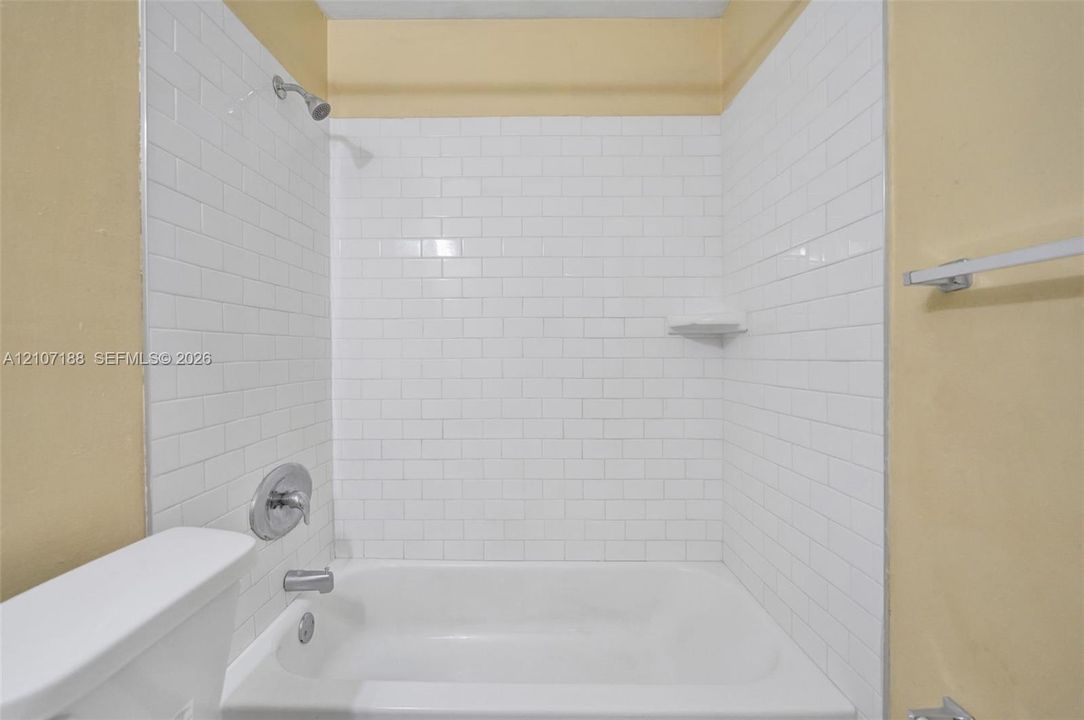 Bathtub enclosure featuring white subway tile surround, integrated soap dish, chrome shower head, and chrome mixing valve