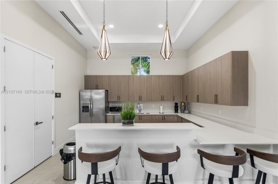 Kitchen featuring flat-panel wood-finish cabinetry, white countertops, stainless steel appliances, geometric pendant lighting, and a tray ceiling