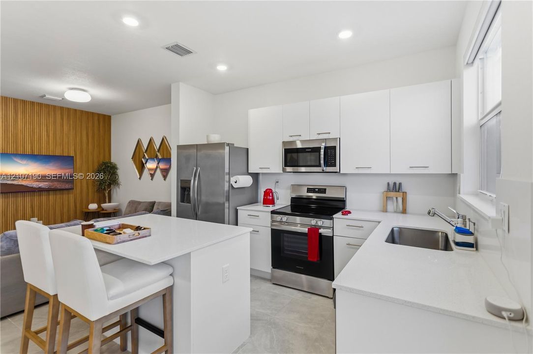 Kitchen featuring white cabinetry, quartz countertops, stainless steel appliances, a central island with integrated seating, and recessed ceiling lighting