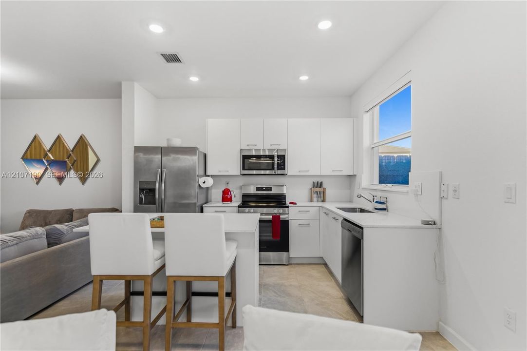 Kitchen featuring white flat-panel cabinetry, white solid-surface countertops, stainless steel appliances, a peninsula with bar seating, and recessed lighting