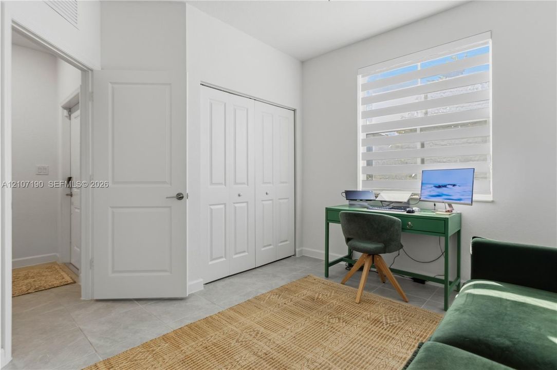 Room featuring light-toned tile flooring, dual-panel interior doors, a double-door closet with recessed hardware, and a window equipped with banded light-filtering shades