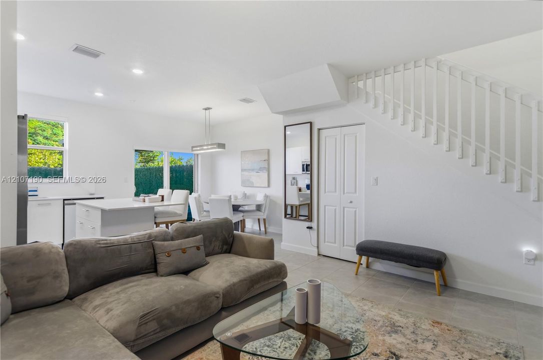 Open-concept interior featuring neutral tile flooring, recessed lighting, a central kitchen island, and a staircase with white vertical balusters