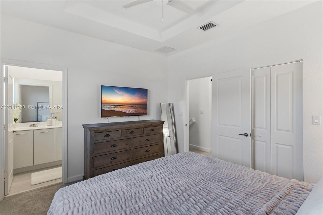Room featuring a tray ceiling with a central ceiling fan, neutral carpeting, and a double-door closet
