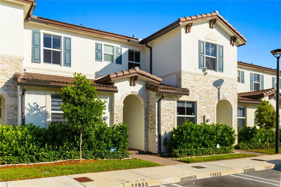 Stucco exterior featuring stacked stone accents, decorative shutters, clay tile roof detailing, and arched entryway