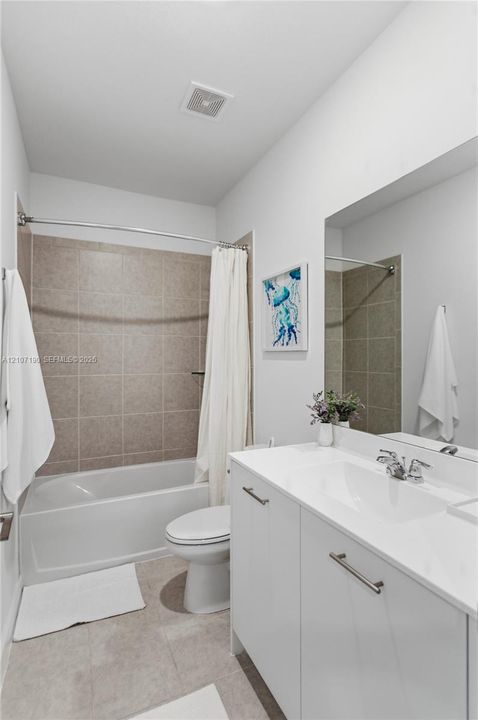 Bathroom featuring a white vanity with a composite countertop and integrated sink, chrome faucet hardware, a large wall-mounted mirror, and a tub with a tile surround