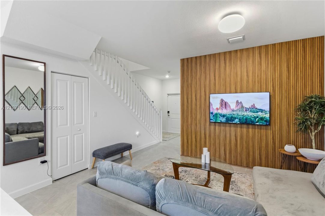 Interior featuring a vertical wood-slat accent wall, tile flooring, white staircase railing, flush-mount ceiling lighting, and a wall-mounted full-length mirror