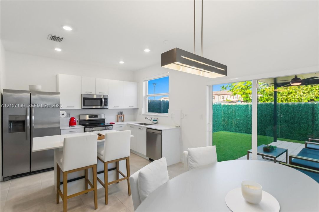 Kitchen featuring white cabinetry, quartz countertops, stainless steel appliances, a modern rectangular pendant light, and sliding glass doors to a covered patio