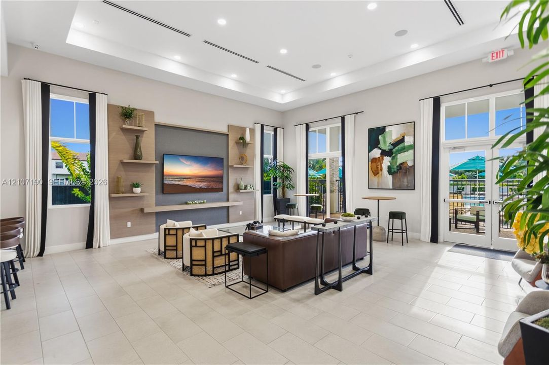 Spacious common area featuring recessed tray ceiling lighting, large-format tile flooring, a custom media wall with built-in shelving, and floor-to-ceiling glass-paned doors