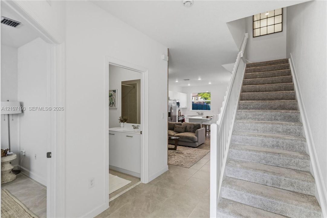 Foyer featuring large-format tile flooring, a carpeted staircase with white railings, and a grid-style accent window