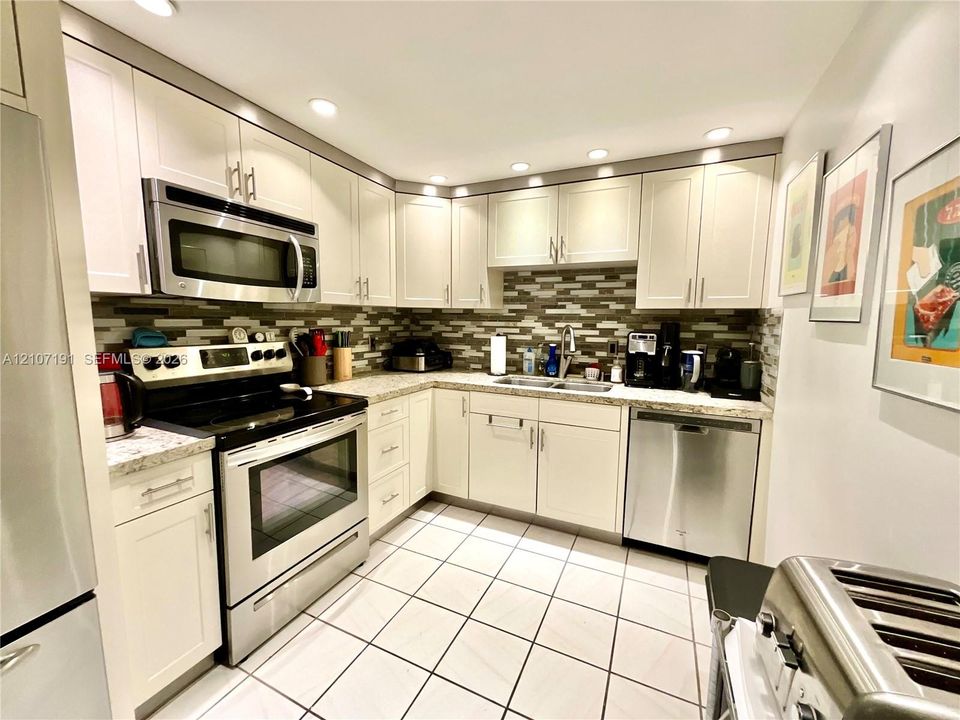 Kitchen featuring shaker-style cabinetry, stainless steel appliances, speckled stone-finish countertops, decorative multi-tone tile backsplash, and recessed lighting