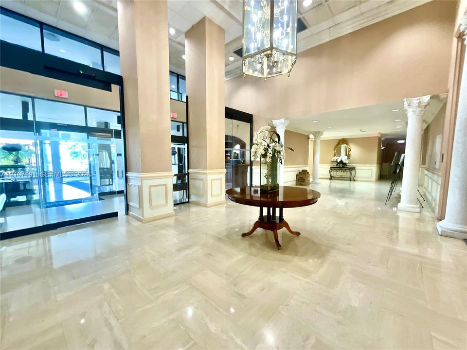 Grand lobby featuring high ceilings, stone flooring in a herringbone pattern, decorative columns, wainscoting, and a hanging pendant chandelier