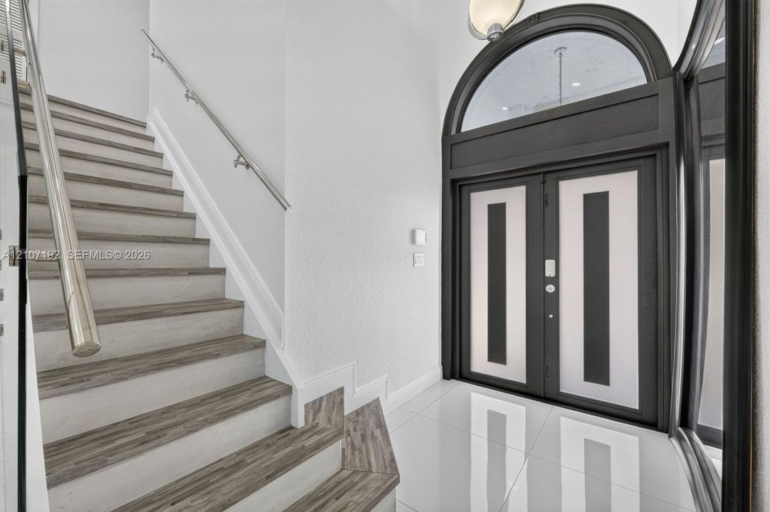 Double-door entryway featuring a decorative arched transom window, staircase with wood-finish treads, and polished tile flooring