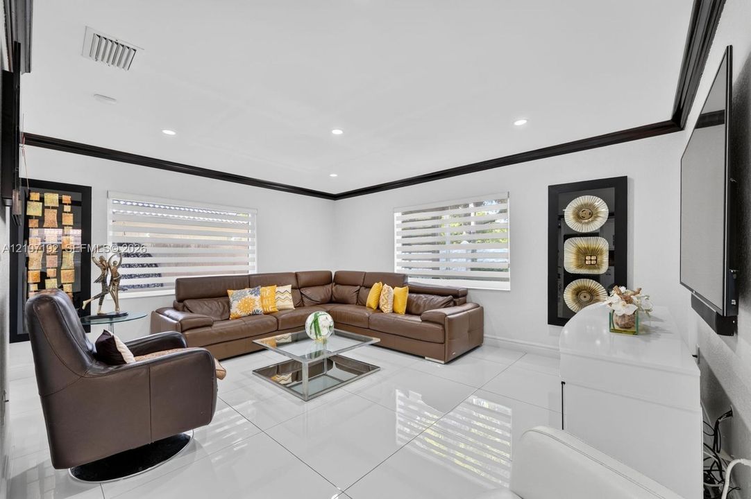 Living area featuring large-format tile flooring, high-contrast black crown molding, recessed lighting, and dual-layered horizontal window blinds