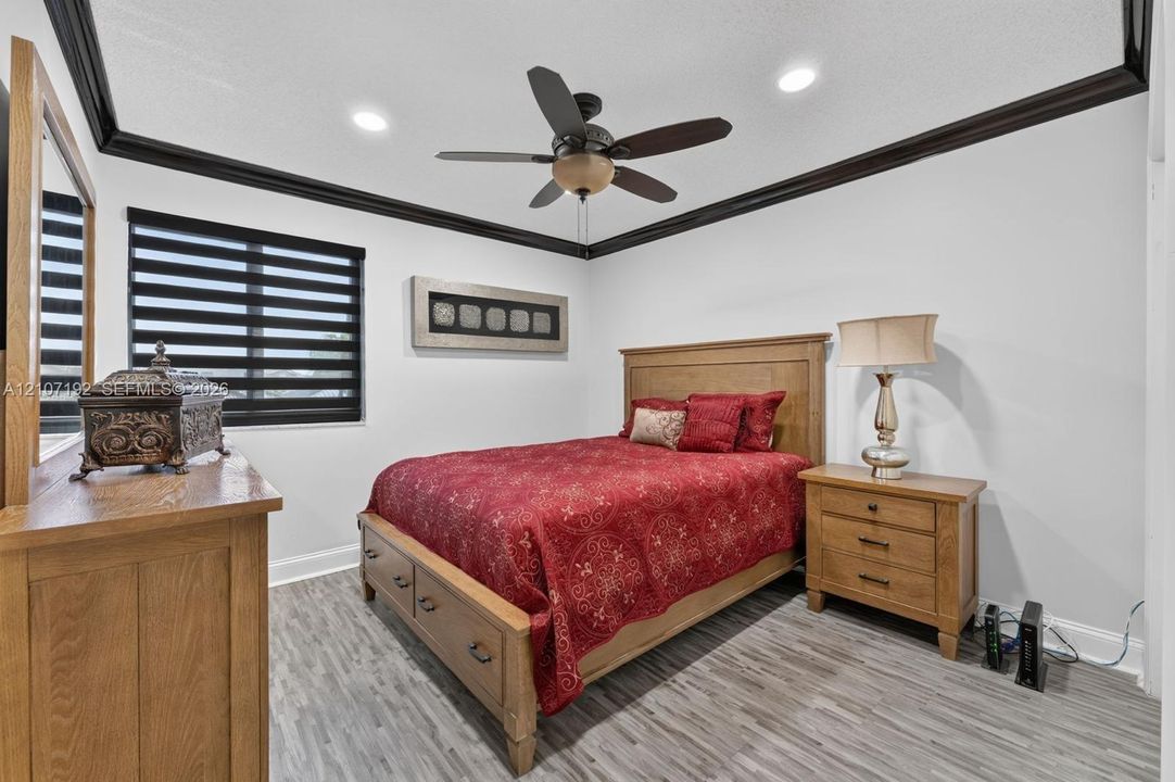 Tray ceiling with dark crown molding, wood-finish flooring, recessed lighting, and a ceiling fan