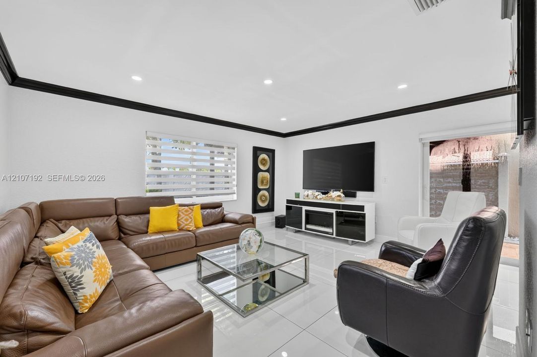 Living space featuring high-gloss tile flooring, crown molding, recessed lighting, and dual-shade window treatments