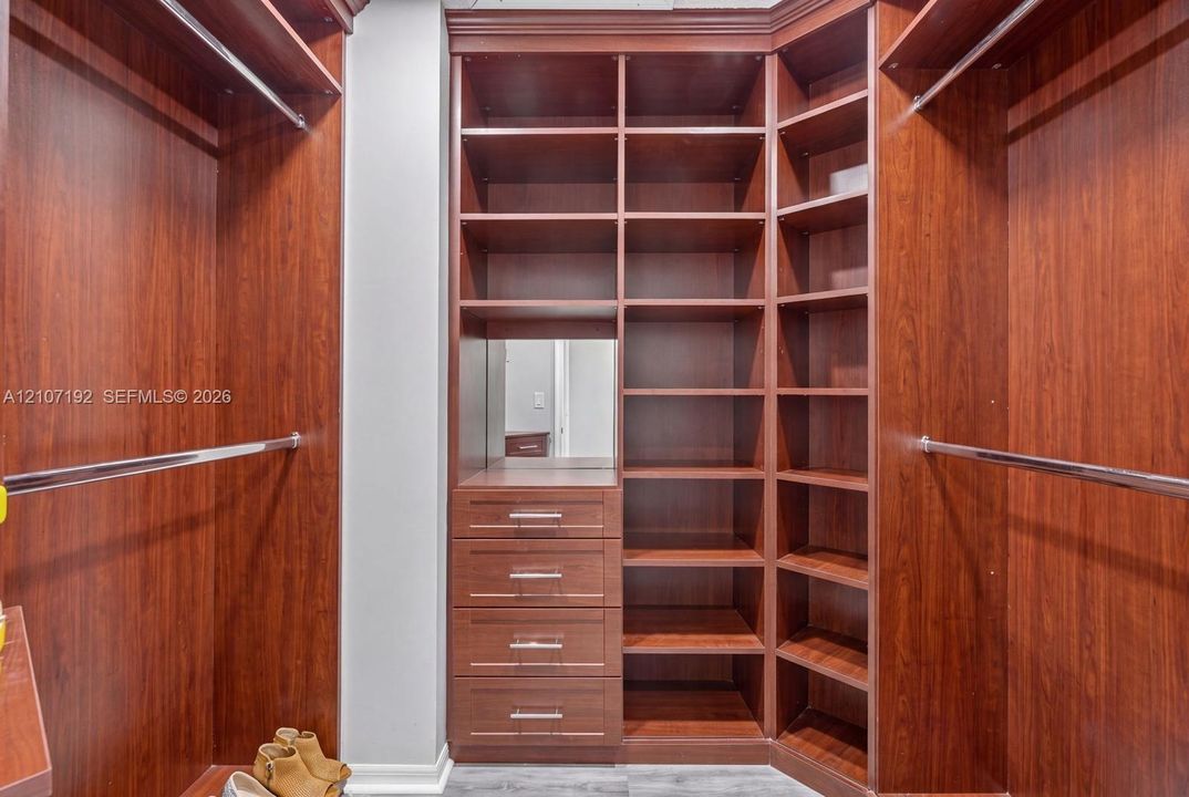 Custom walk-in closet featuring wood-finish cabinetry, built-in shelving, four integrated drawers with metal pulls, and dual stainless steel hanging rods