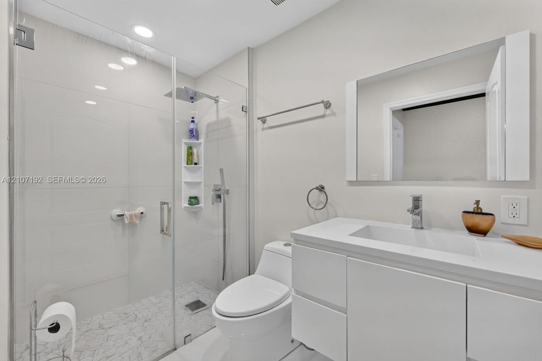 Modern bathroom featuring a frameless glass shower enclosure, rainfall shower head with handheld wand, integrated storage niche, sleek white vanity with a rectangular sink, and recessed lighting