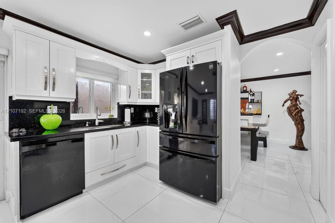 Kitchen featuring white shaker-style cabinetry, black stone countertops, high-contrast black appliances, crown molding, and polished tile flooring