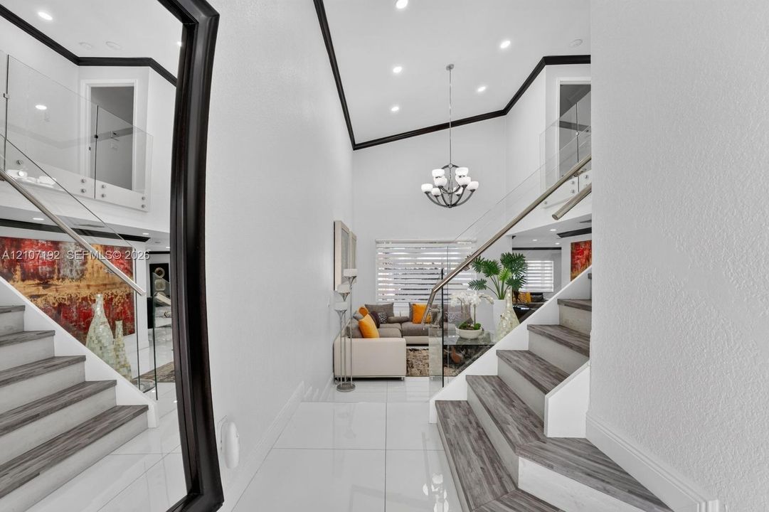 Two-story foyer featuring high ceilings, large-format tile flooring, a multi-tier chandelier, staircase with wood-finish treads, and glass panel railings