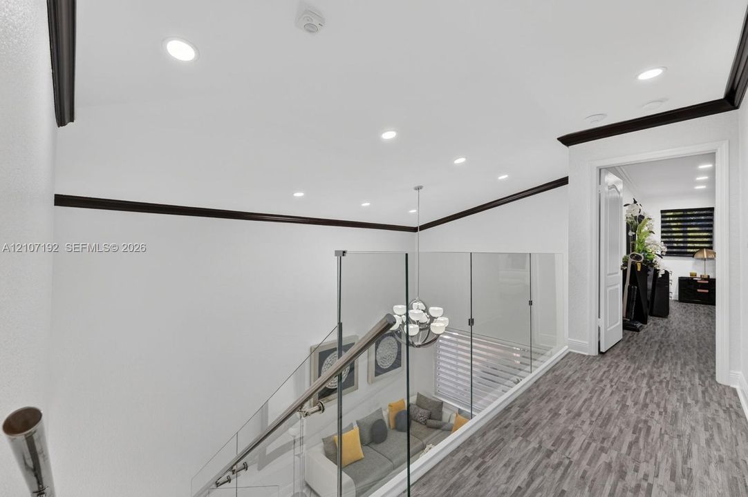 Interior landing featuring wood-finish flooring, glass panel railing with a metallic handrail, recessed ceiling lighting, and dark-toned crown molding