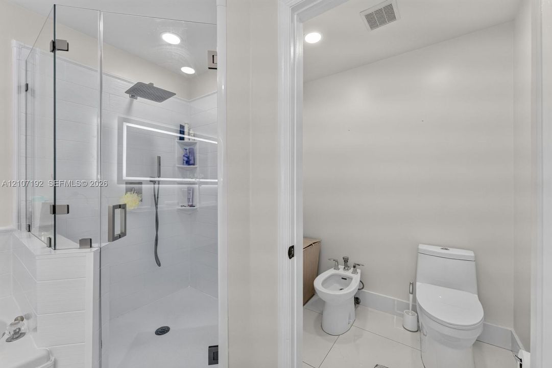 Glass-enclosed shower with rainfall showerhead, integrated LED lighting, built-in shelving, bidet, and elongated commode