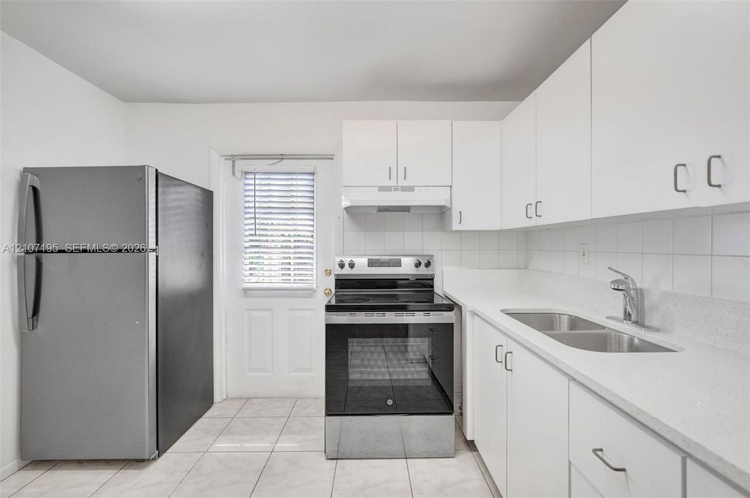 Kitchen featuring white cabinetry, solid-surface countertops, stainless steel appliances, tile backsplash, and ceramic tile flooring