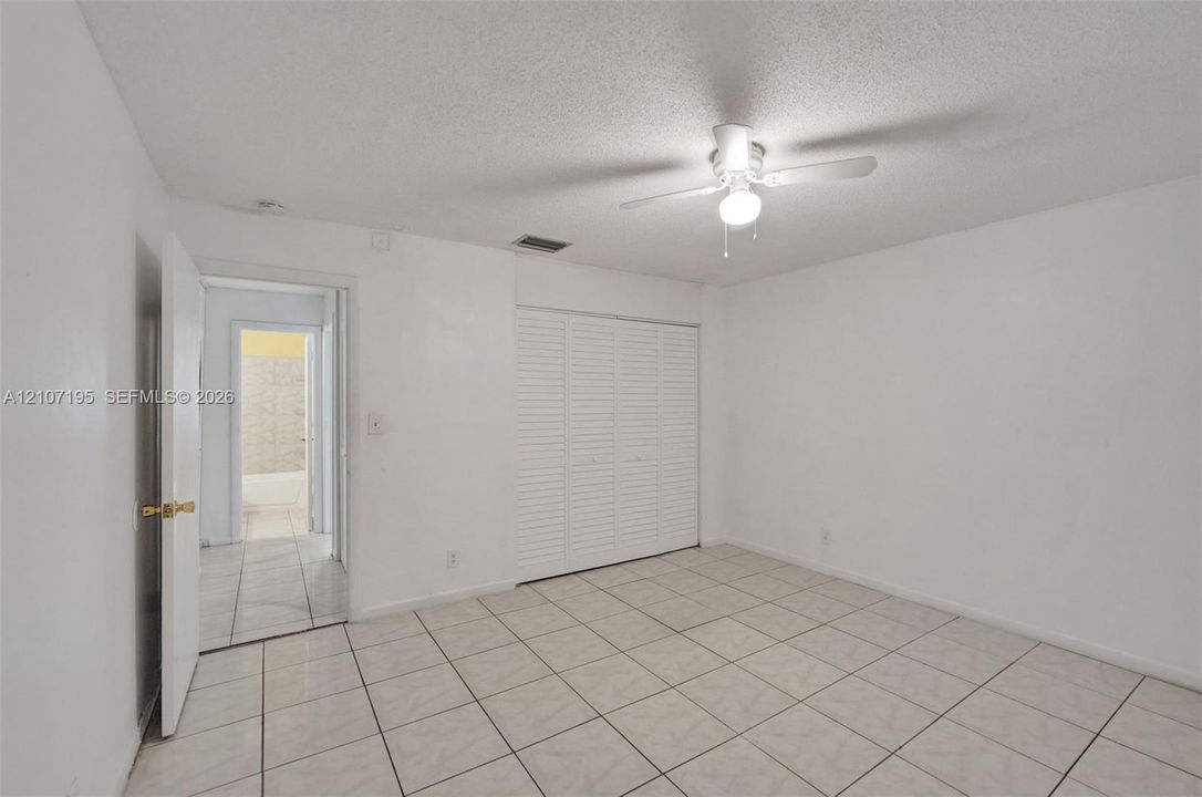 Tile flooring, ceiling-mounted light fixture with fan, and white louvered closet doors