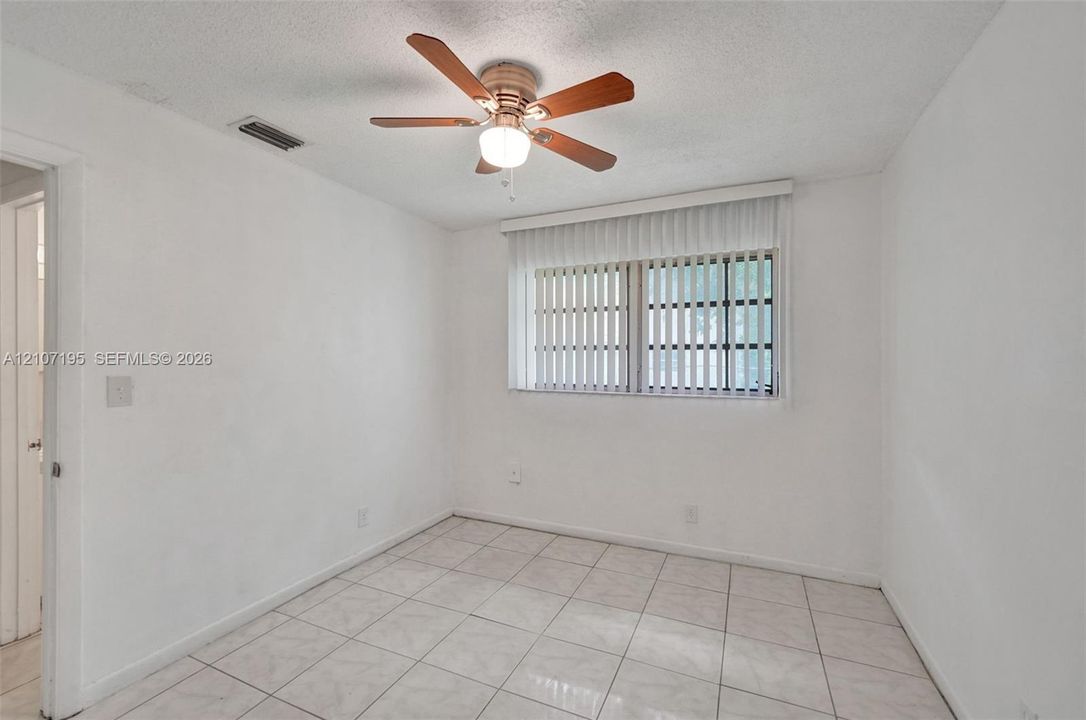 Room interior featuring neutral tile flooring, a multi-blade ceiling fan with integrated lighting, and vertical window blinds