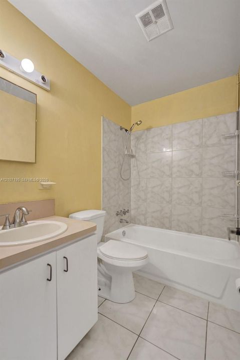 Bathroom featuring white cabinetry, integrated sink, tiled tub surround, and tile flooring