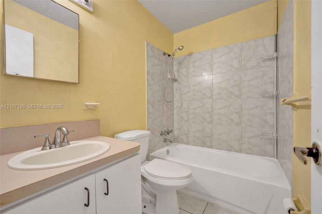 Bathroom featuring a white vanity cabinet with a solid surface countertop, integrated sink with chrome faucet, tub-shower combination with tile surround, and a wall-mounted mirror