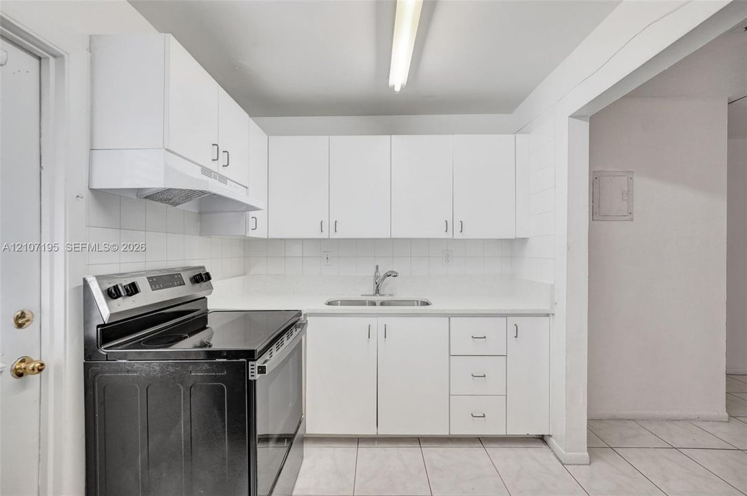 Kitchen featuring white cabinetry, solid-surface countertops, dual-basin stainless steel sink, tile backsplash, and a black electric range
