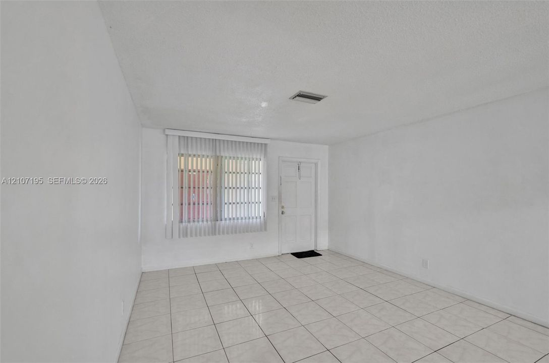 Interior space featuring light-toned ceramic tile flooring, vertical window blinds, and a solid-panel door
