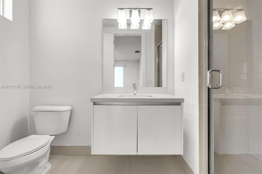 Floating vanity with an integrated countertop, large frameless wall-mounted mirror, three-light frosted glass fixture, and glass-enclosed shower