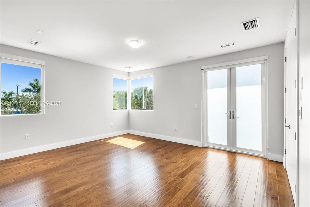Room featuring wood-finish flooring, recessed lighting, double French doors, and windows with exterior greenery