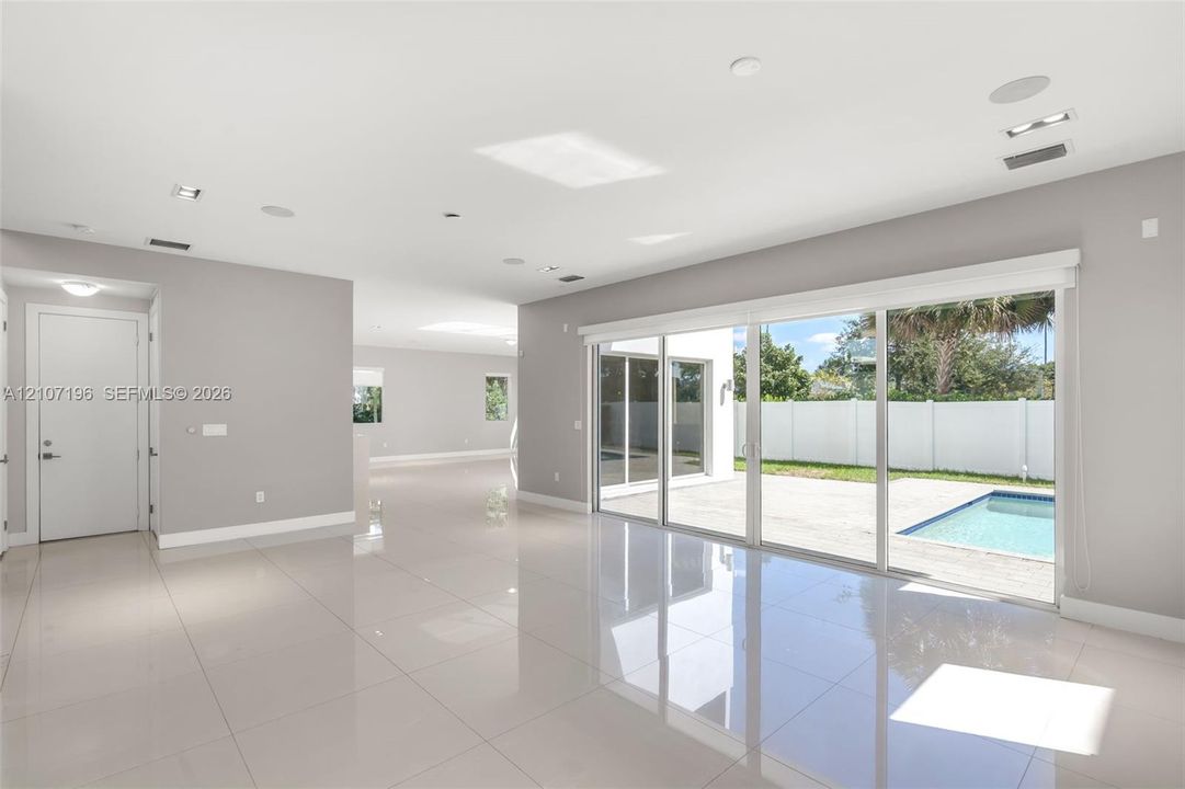 Large format tile flooring, recessed lighting, ceiling-mounted speakers, and expansive floor-to-ceiling glass sliding doors opening to a concrete patio and swimming pool