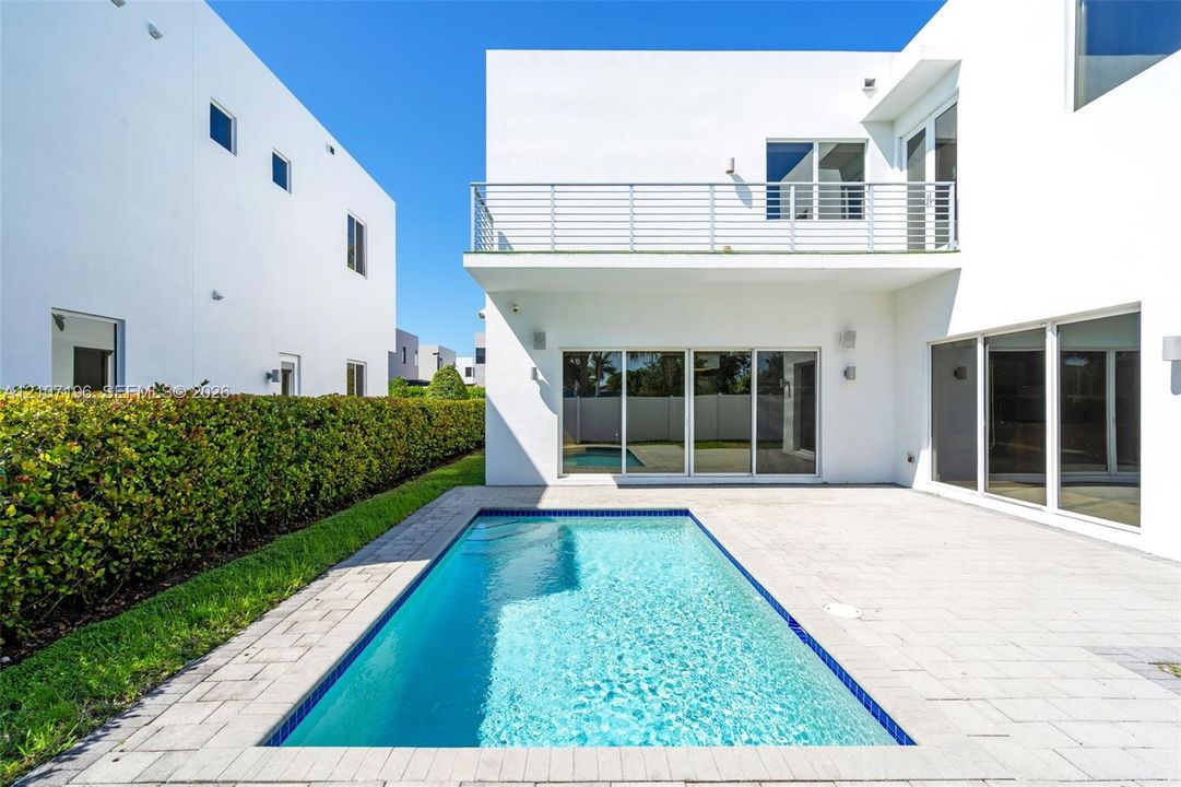 Contemporary exterior featuring a private swimming pool, concrete paver patio, second-story balcony with metal railing, and expansive glass sliding doors