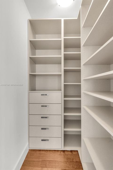 Customized built-in storage system featuring floor-to-ceiling shelving, five soft-close drawers with metallic pulls, and wood-finish flooring