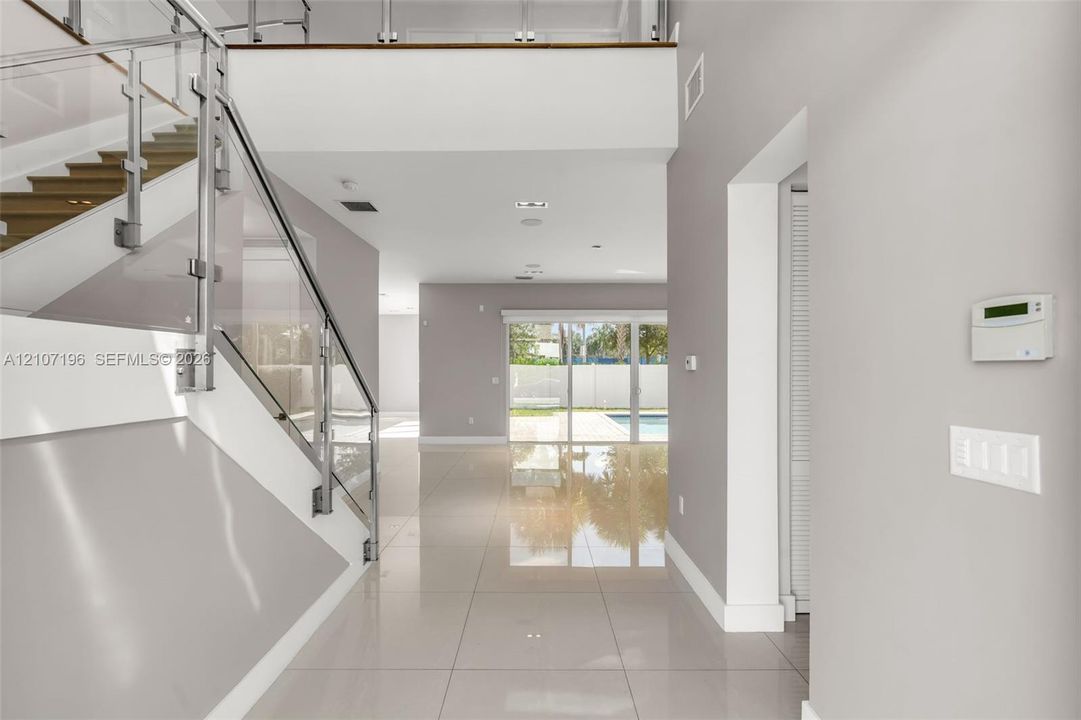 Open-concept foyer featuring oversized light-toned tile flooring, a glass-panel staircase railing, and double-height ceilings