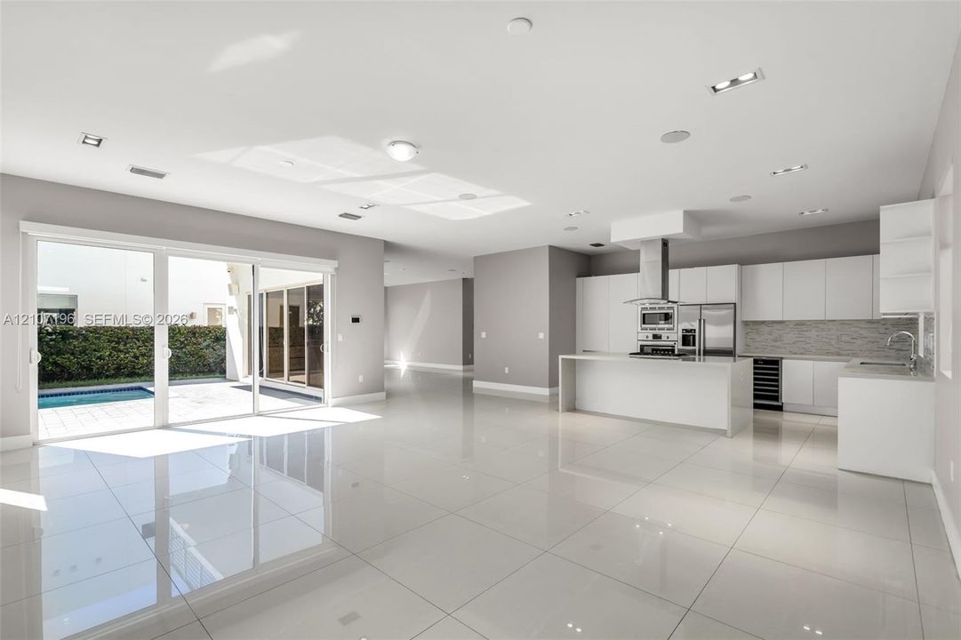 Open-concept space featuring polished tile flooring, white slab-front cabinetry, a kitchen island with stone-surface countertop, built-in stainless steel appliances, and large-format sliding glass doors