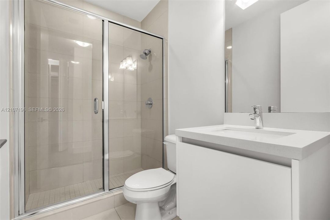 Bathroom featuring a sliding glass shower door, floor-to-ceiling wall tile, white vanity with a solid-surface countertop, and a built-in mirror