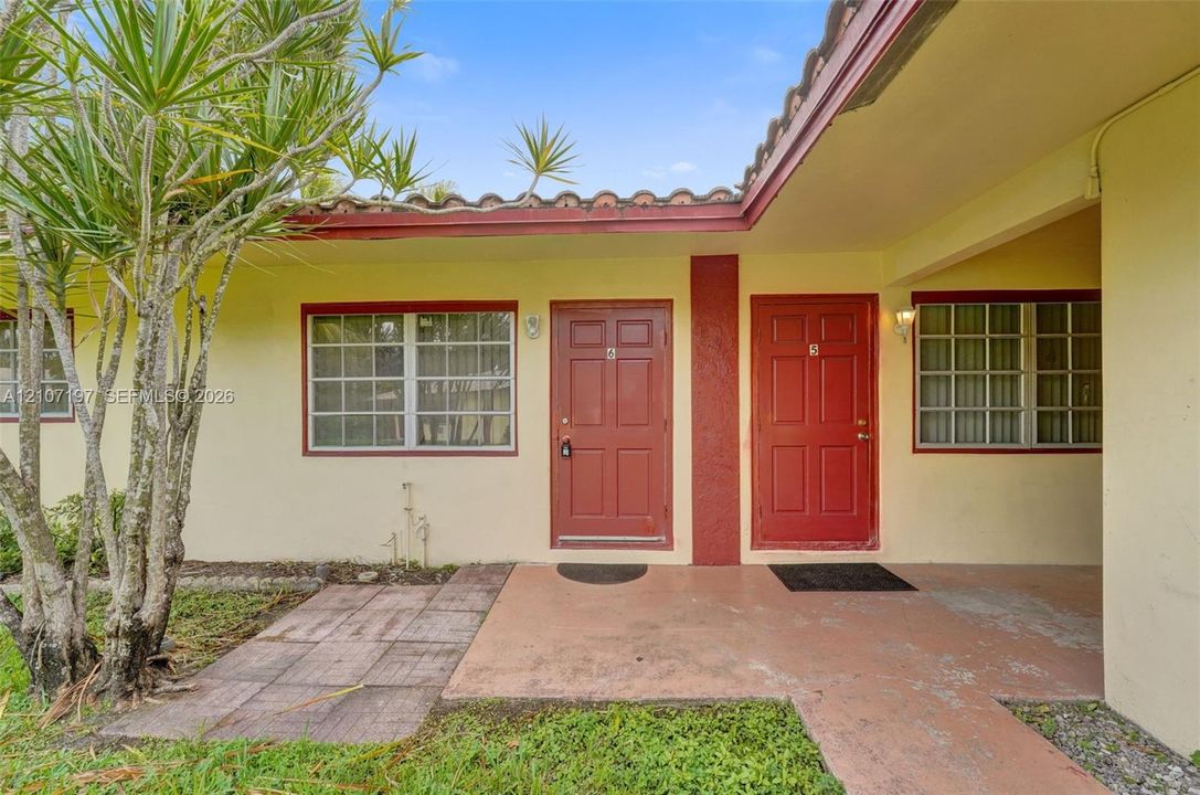 Stucco exterior featuring clay tile roofing, concrete walkway, and double entry doors with grid-pattern windows