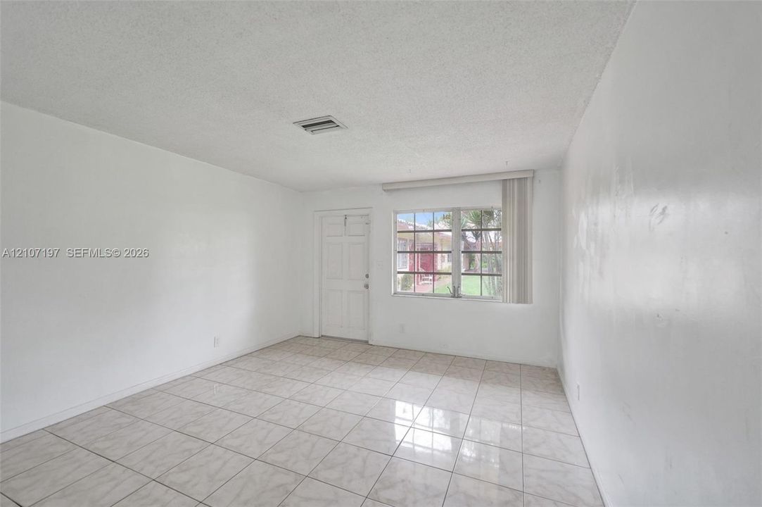 Interior space featuring large-format neutral floor tiling, textured ceiling finish, and a multipane window with vertical blinds
