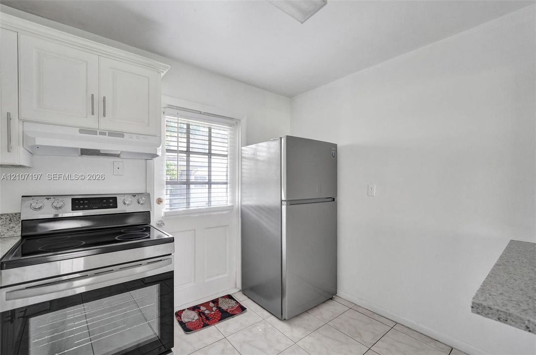 Kitchen featuring white cabinetry, stainless steel electric range with hood, stone-finish countertops, and light-toned tile flooring